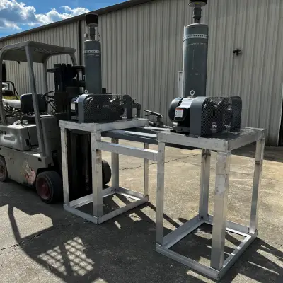 Forklift lifting a metal frame structure with two large industrial motors on it, positioned outdoors near a warehouse.